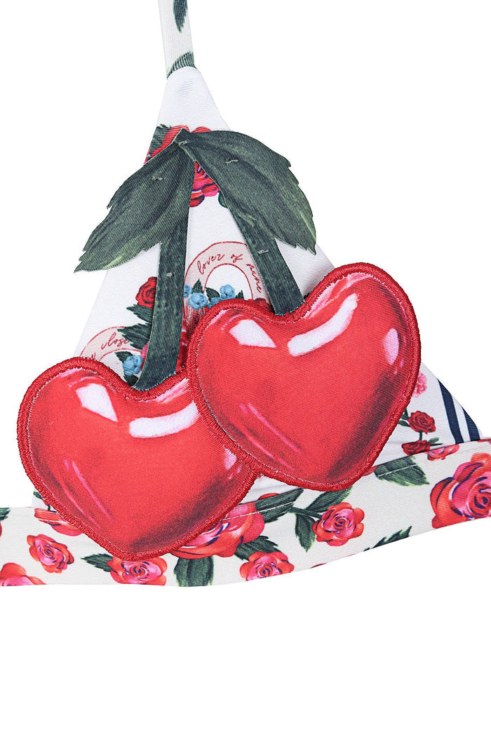White two-piece bikini with red heart-shaped cherry appliqués on top and pattern detail print bottom with roses and striped details