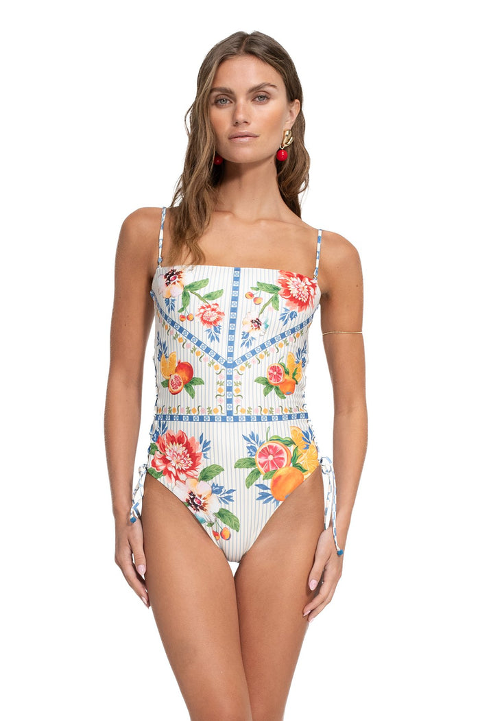 White one-piece swimsuit with vertical pinstripes, pattern detail and citrus fruit print, blue geometric trim, and side lace-up closures