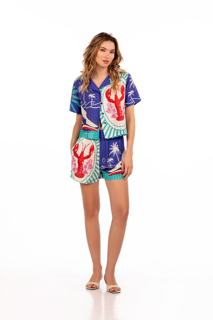 Blue short-sleeve shirt with vibrant placement print featuring lobster illustrations, palm trees, striped accents, and nautical graphics