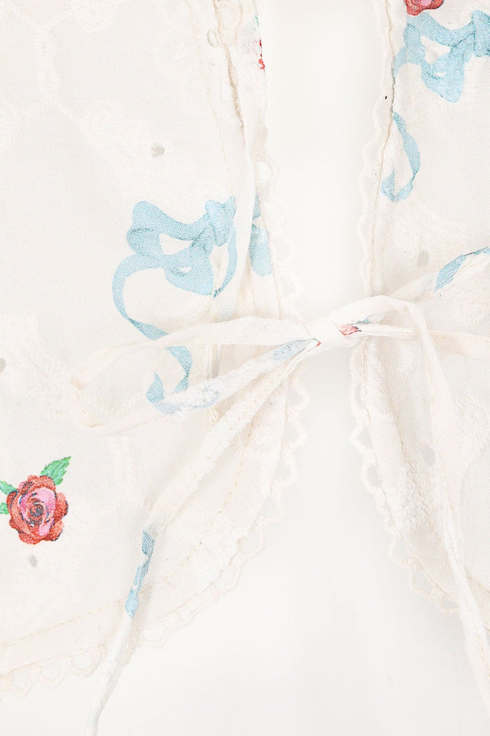 White eyelet shirt with blue embroidered scrollwork and scattered coral pattern detail embroidery, featuring tie-bow front closure