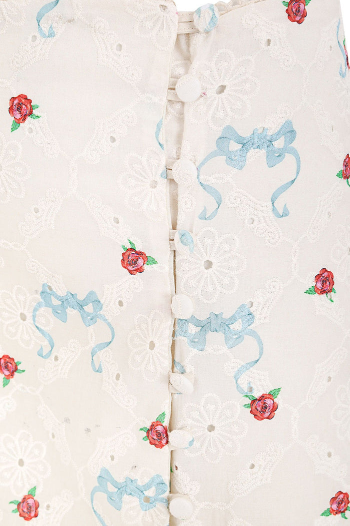 Sarahi maxi skirt in cream eyelet fabric with scattered red rose embroidery and blue ribbon bow print, side button closure with trim details