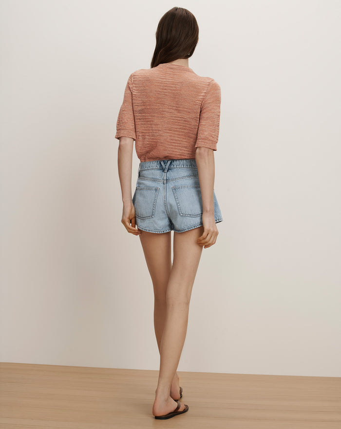 Veronica Beard A woman wears a peach short-sleeve knit top and light wash denim shorts.