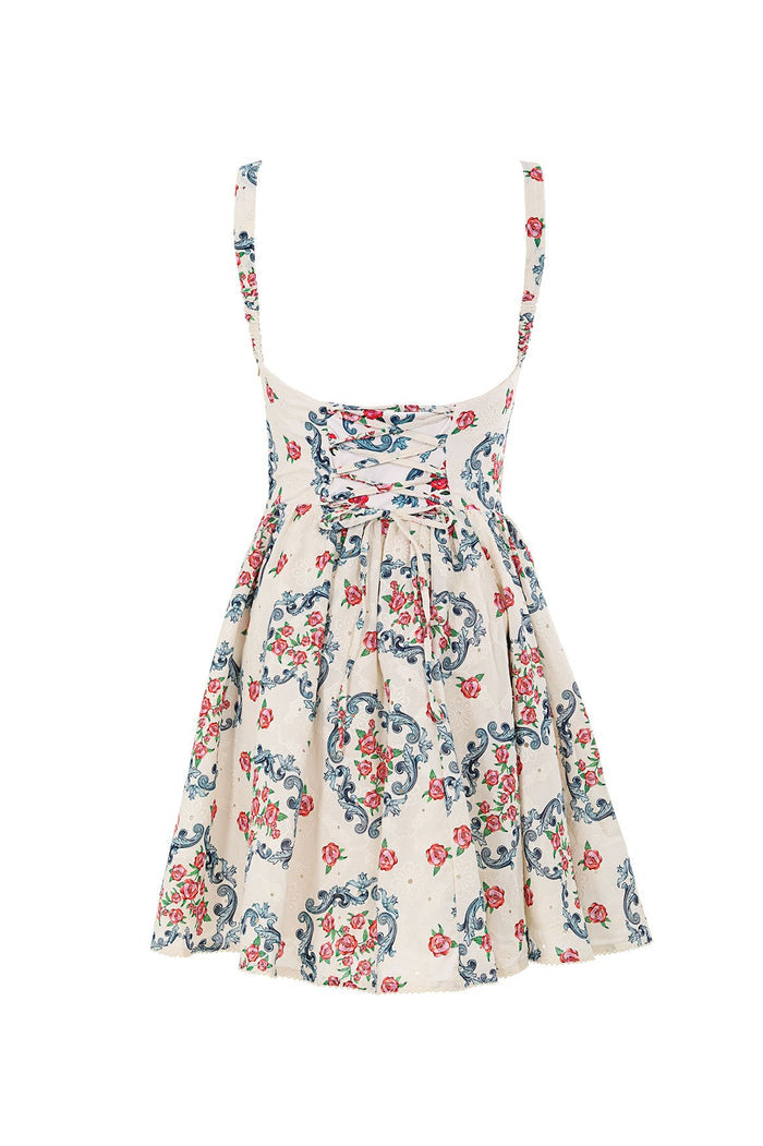 Cream mini dress with adjustable straps, fitted bodice, and gathered skirt, featuring blue scrollwork and pink pattern detail print throughout