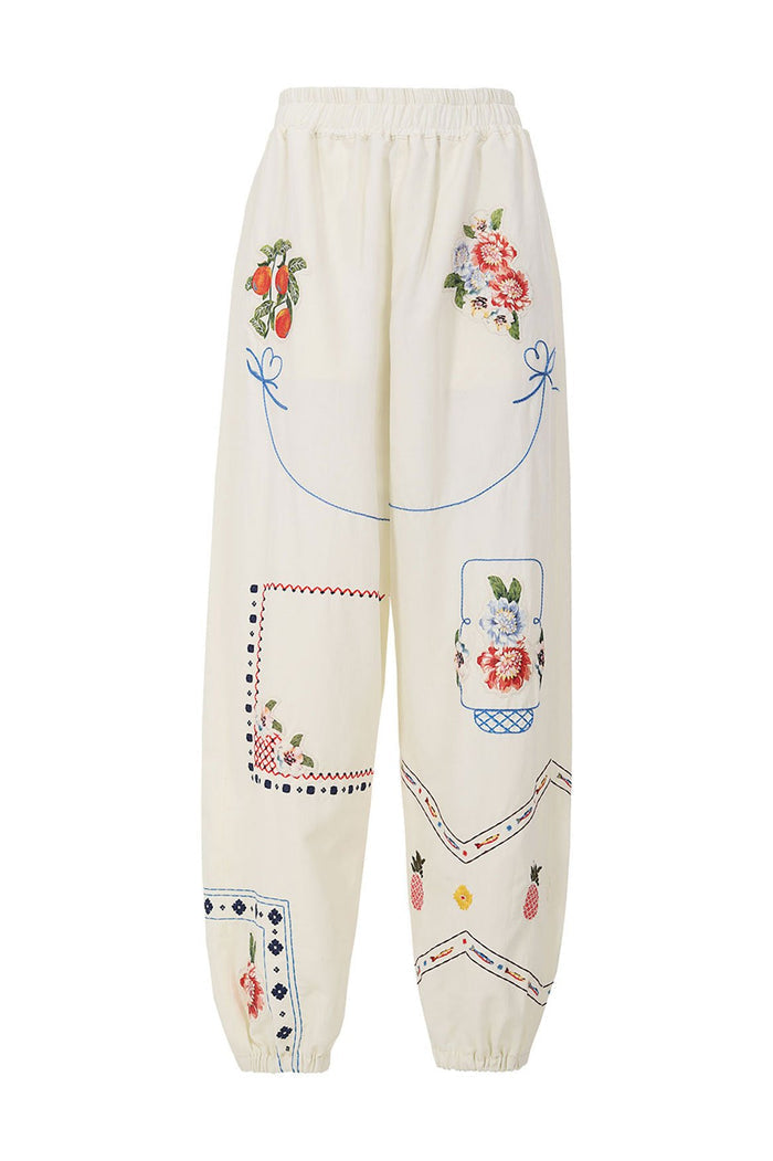 Cream Toscana Pants with elastic waist and cuffs, featuring multicolor embroidered pattern detail blooms, blue outline stitching, and small fruit and…