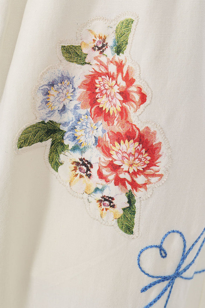 Toscana Pants in cream with beaded pattern detail embroidery featuring coral, blue, and yellow blooms with green leaves, and blue embroidered script…