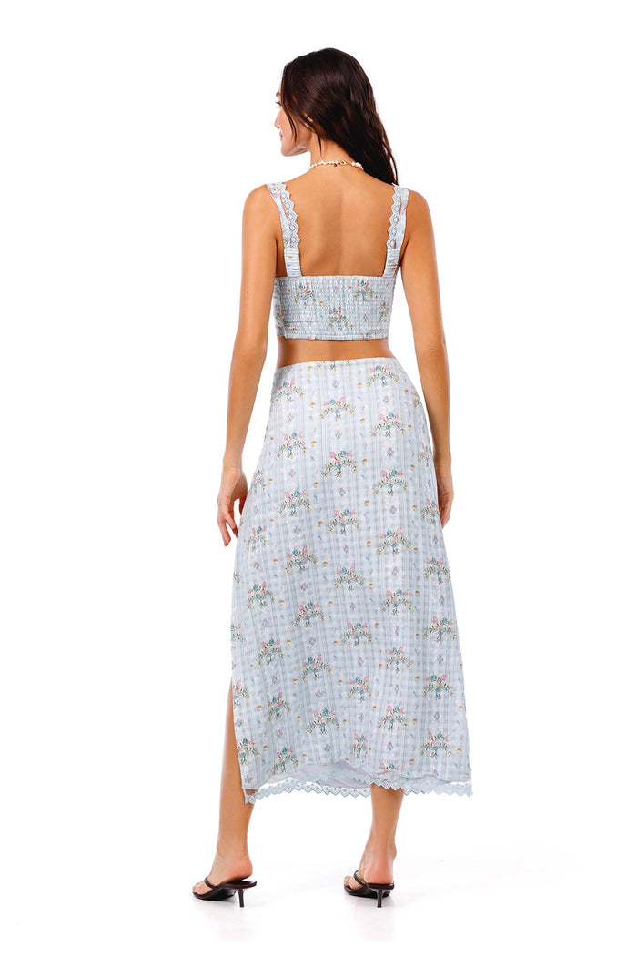 Light blue midi skirt with smocked waistband, pattern detail print, lace trim hem, and side slit, back view