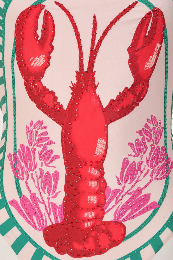 Valmy one piece swimsuit in coral red with embroidered lobster and pink coral embellishments on blush background with green lattice border