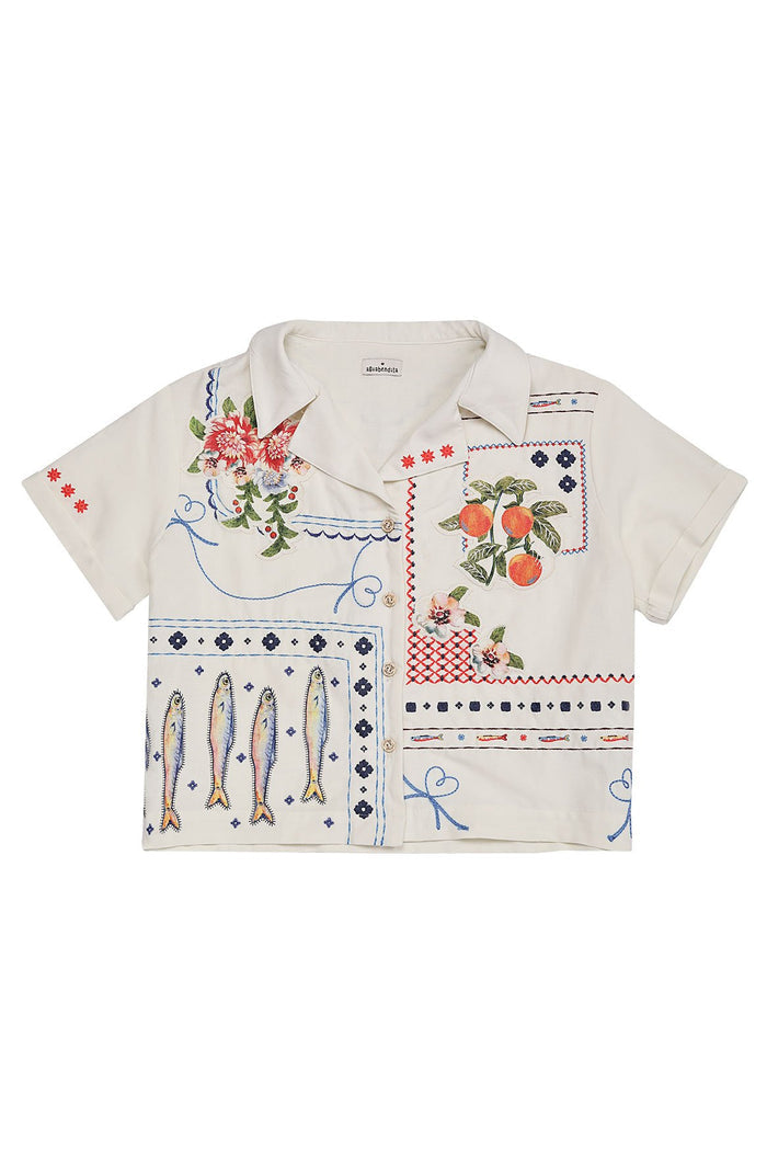 White short-sleeve shirt with multicolor embroidered panels featuring hummingbirds, tropical flowers, oranges, and decorative borders
