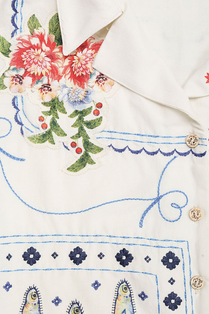 White Vittoria Shirt with embroidered pattern detail bouquets in coral, blue and green, scalloped blue trim, and blue geometric border with decorativ…